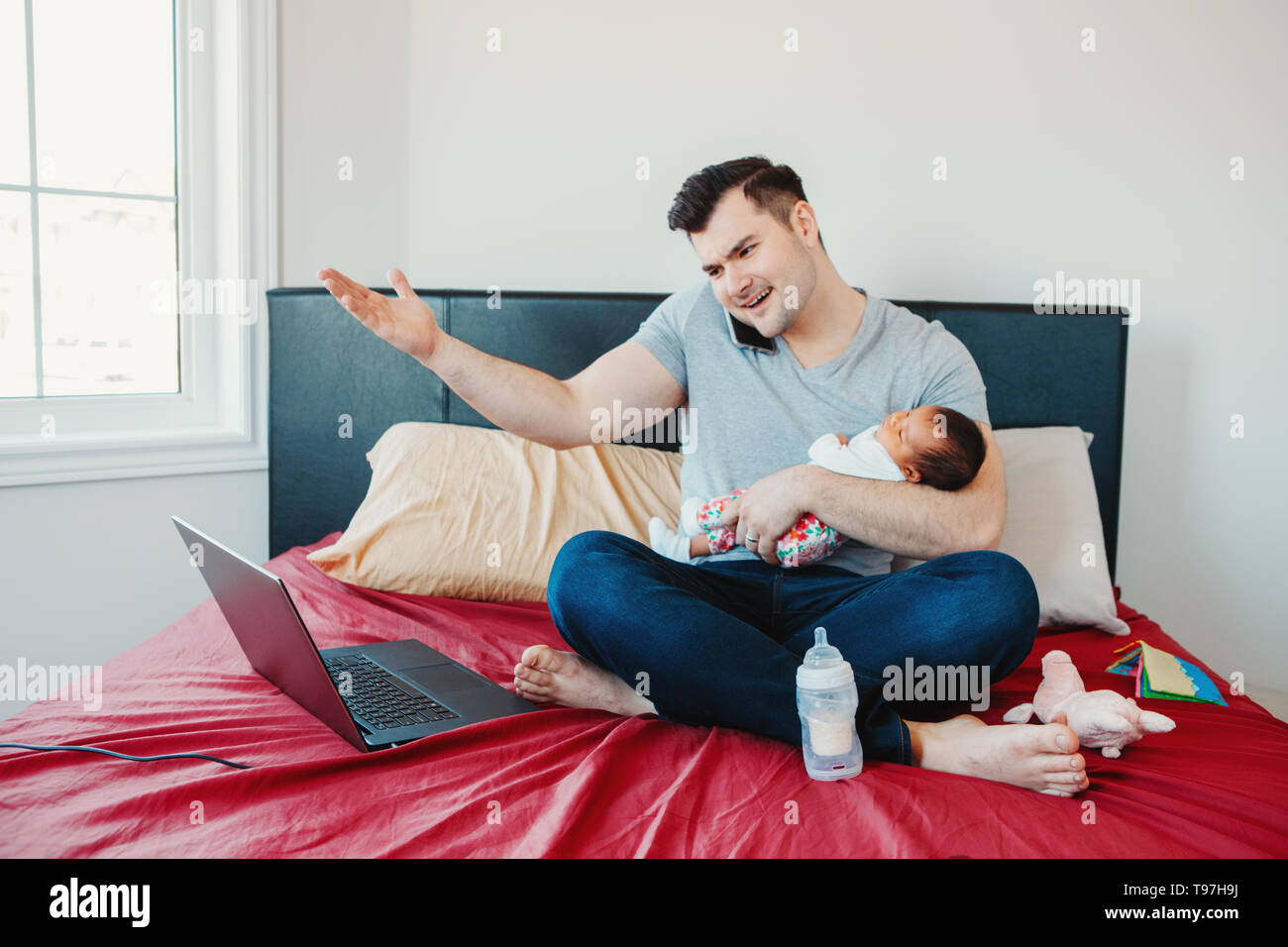 Angry busy Caucasian father with newborn Asian Chinese baby working from home. Male man parent holding child daughter son talking over phone. Single d Stock Photo