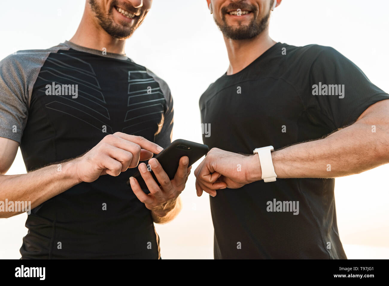 Two twin brothers doing exercises at the beach together, using smart watch Stock Photo