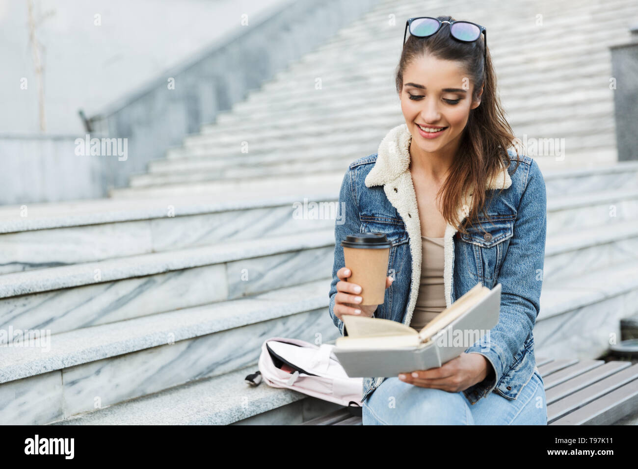 Smiling Young Woman Wearing Jacket Sitting On A Bench Outdoors