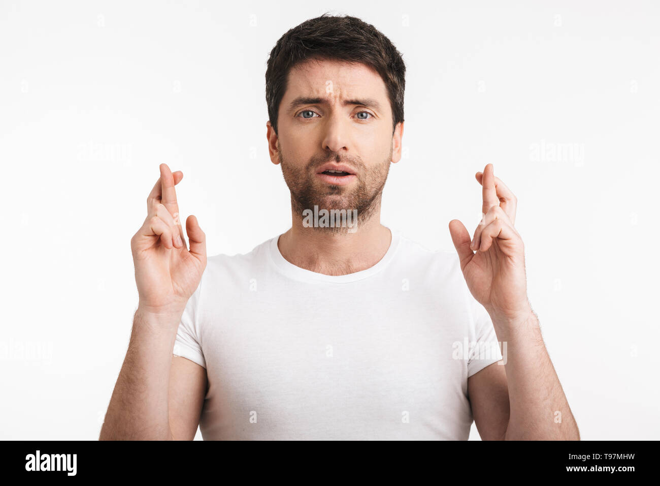 Image of superstitious man 30s with bristle in casual t-shirt keeping fingers crossed and making a wish isolated over white background Stock Photo