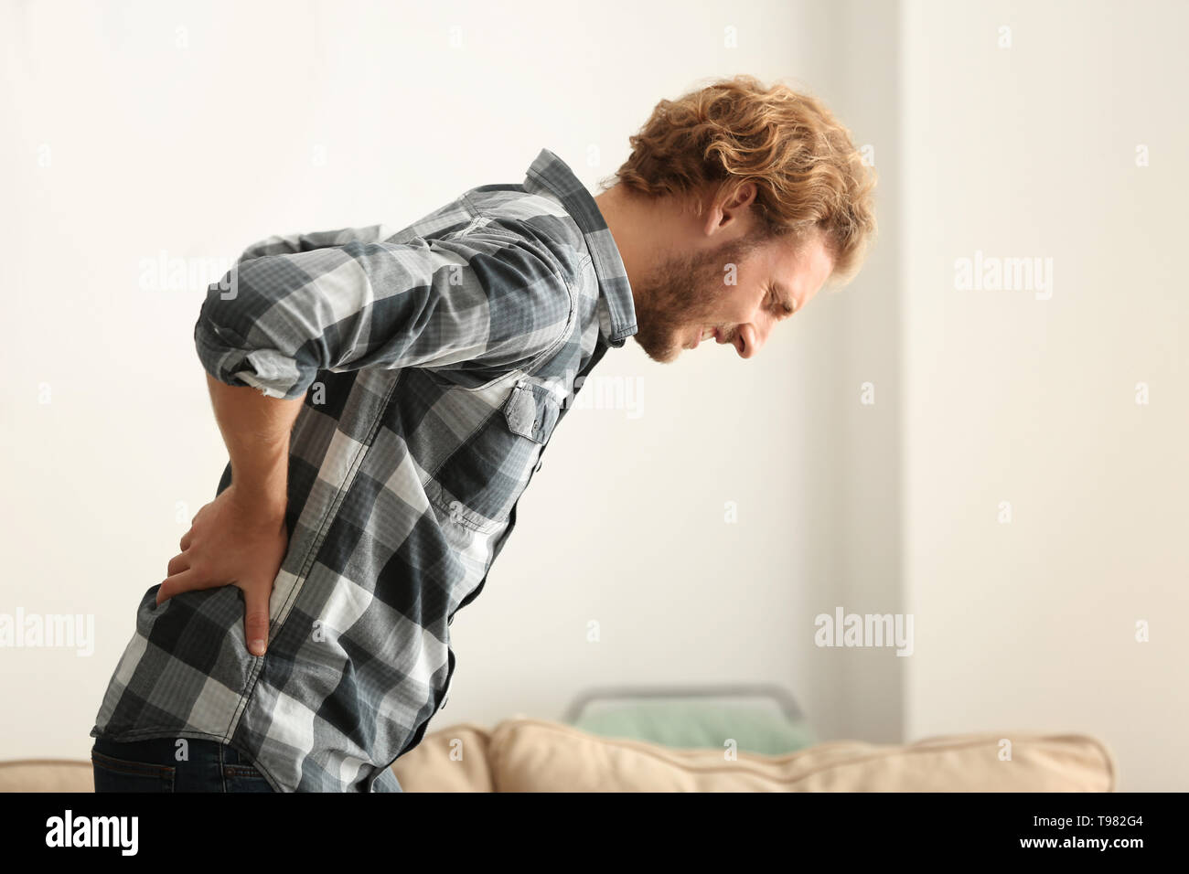 Young man suffering from back pain at home Stock Photo - Alamy
