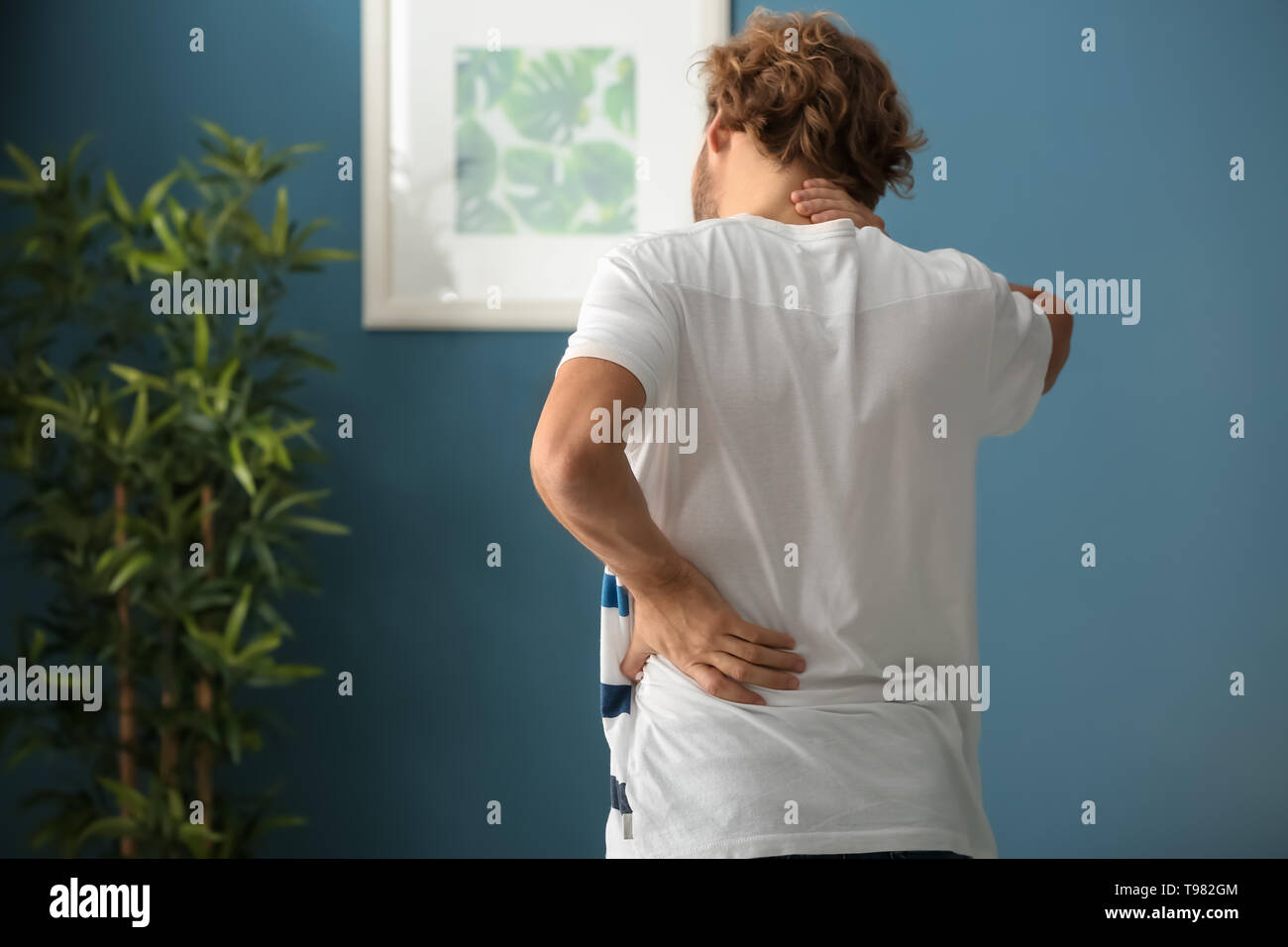Young man suffering from back pain at home Stock Photo - Alamy