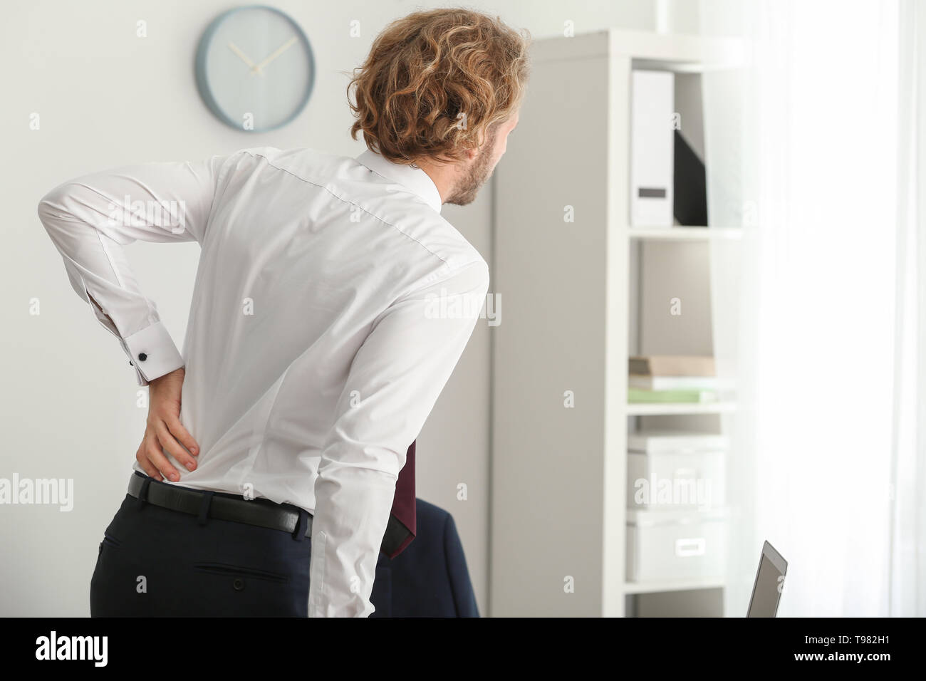 Young businessman suffering from back pain in office Stock Photo - Alamy