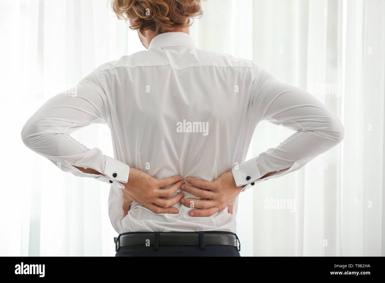 Young businessman suffering from back pain near window Stock Photo Alamy