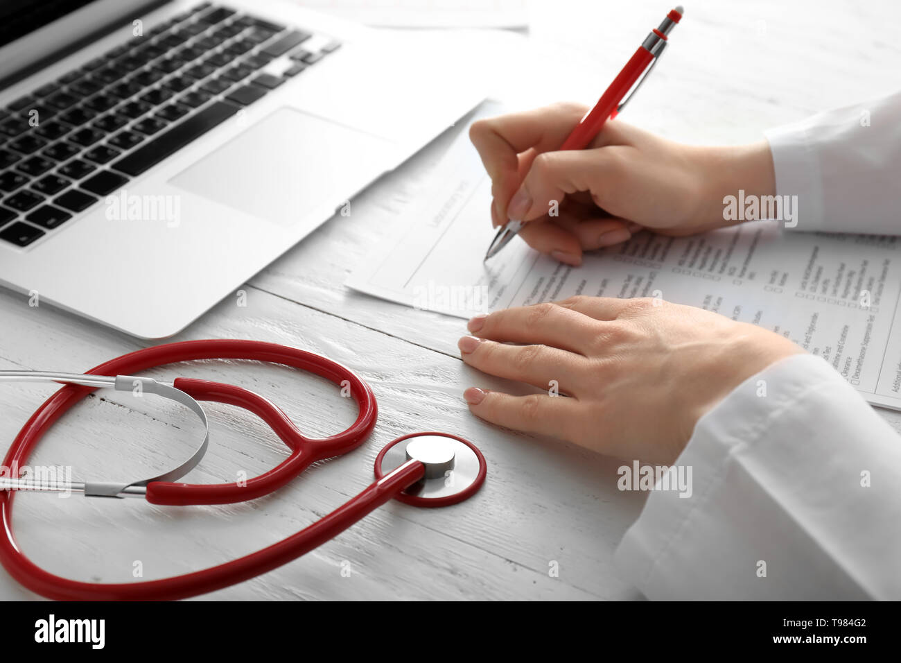 Female doctor filling in laboratory test request form on white table
