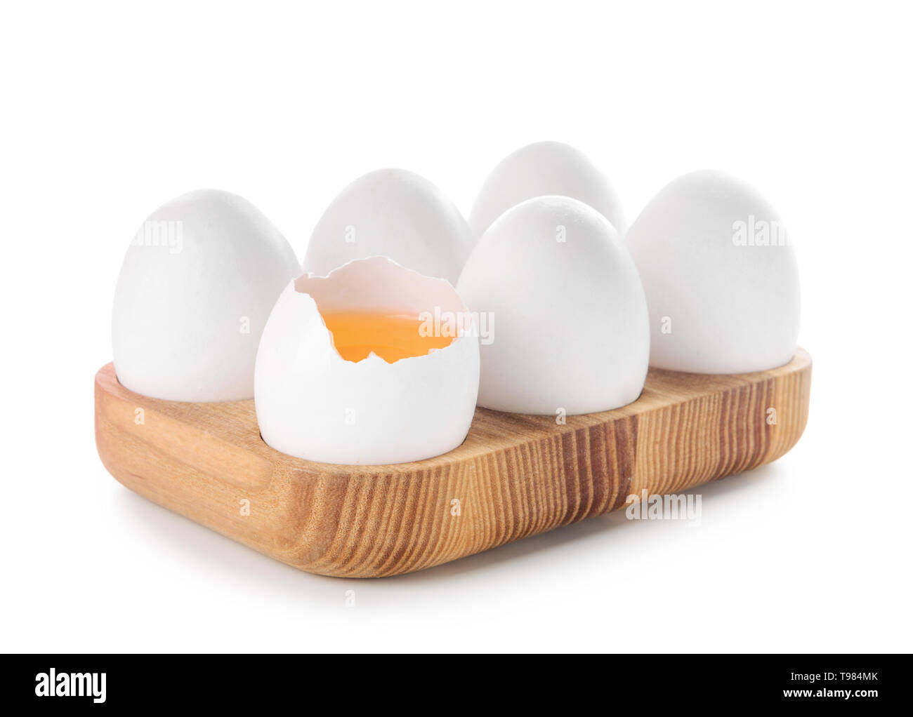 Wooden holder with cracked and whole chicken eggs on white background ...