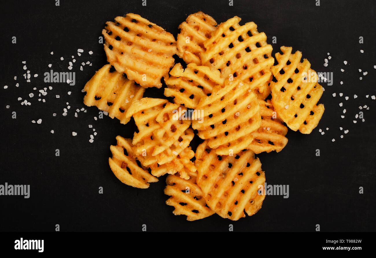 Crispy potato waffles fries, wavy, crinkle cut, criss cross cries on black background Stock Photo