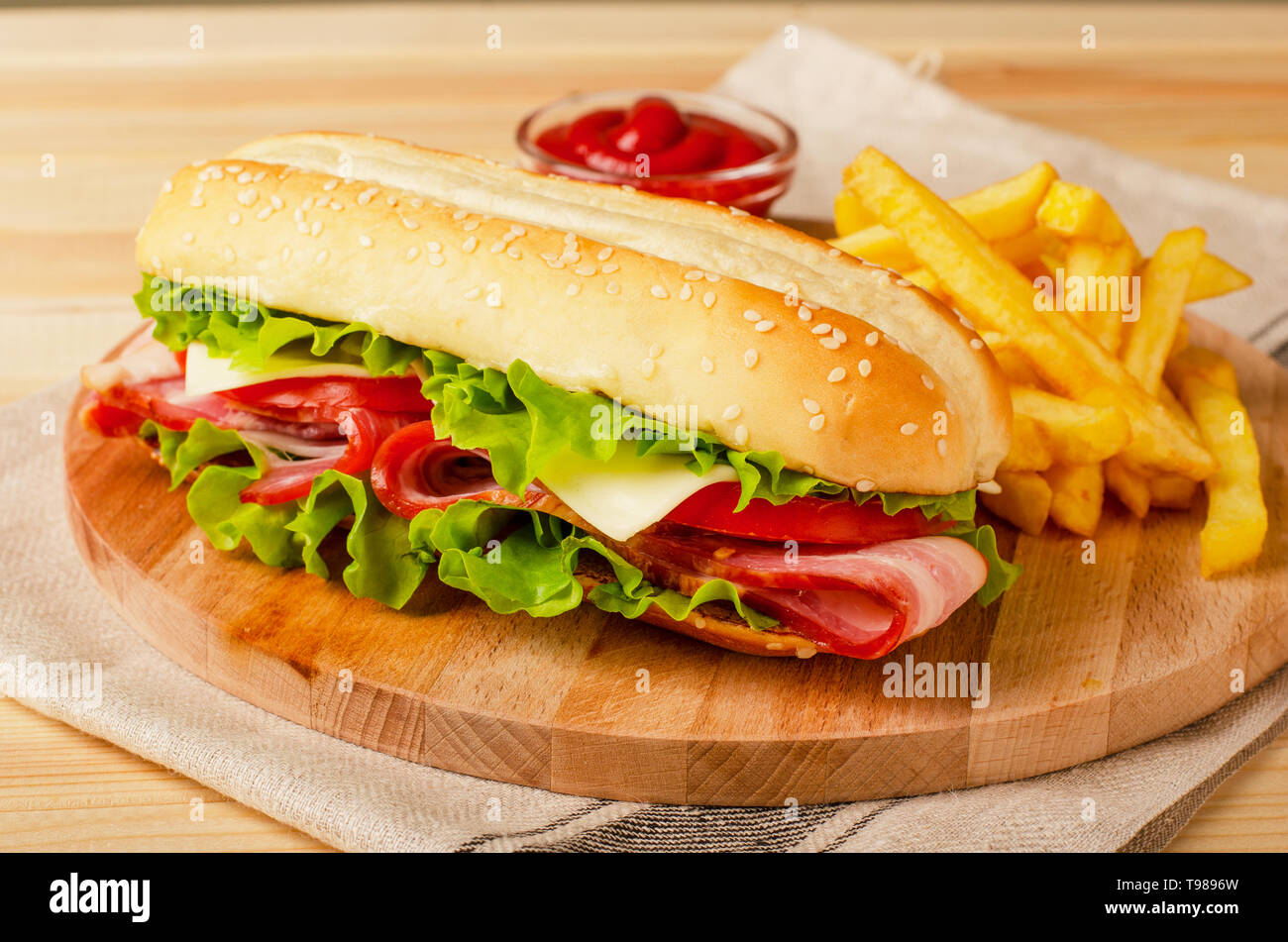 Submarine sandwich with bacon, cheese, tomatoes and lettuce on wooden background Stock Photo