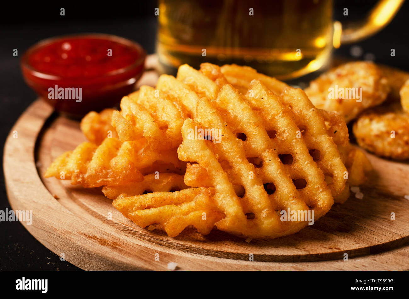 Crispy potato waffles fries, wavy, crinkle cut, criss cross cries with on a cutting board Stock Photo