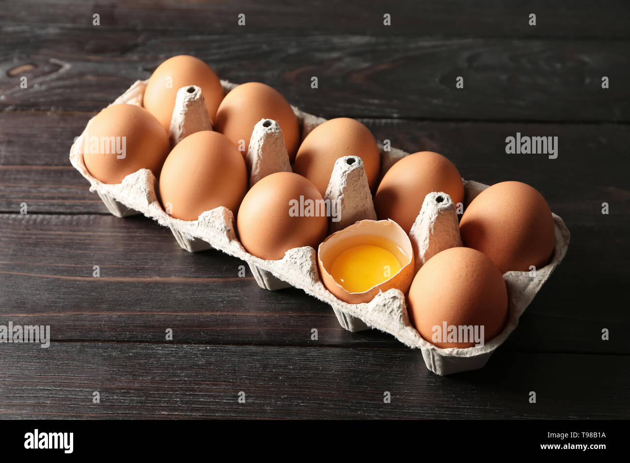 Cracked and whole chicken eggs in carton pack on dark wooden table ...