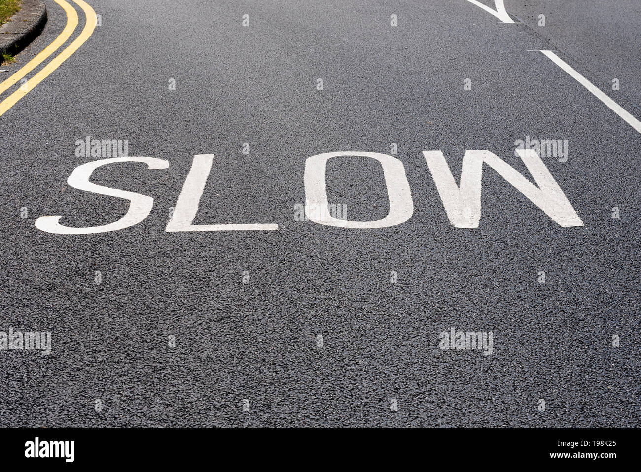 Slow road marking warning sign, freshly painted on recently laid black tarmac. SLOW warning sign road markings painted on road surface. New. Fresh Stock Photo