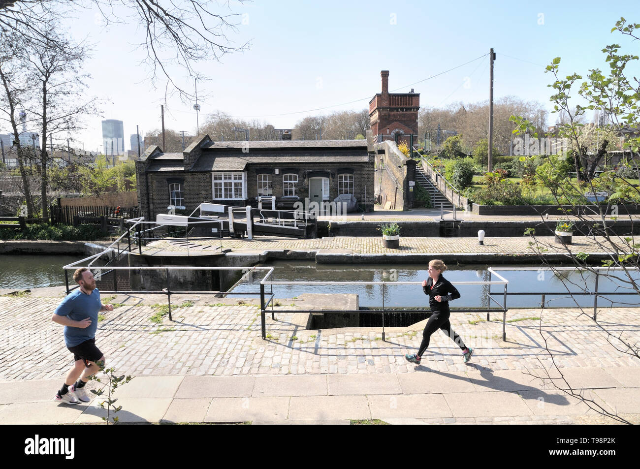 People jogging by St Pancras Lock with Lock Keepers Cottage and Waterpoint in the background, Regent's Canal, King's Cross, London, England, UK Stock Photo