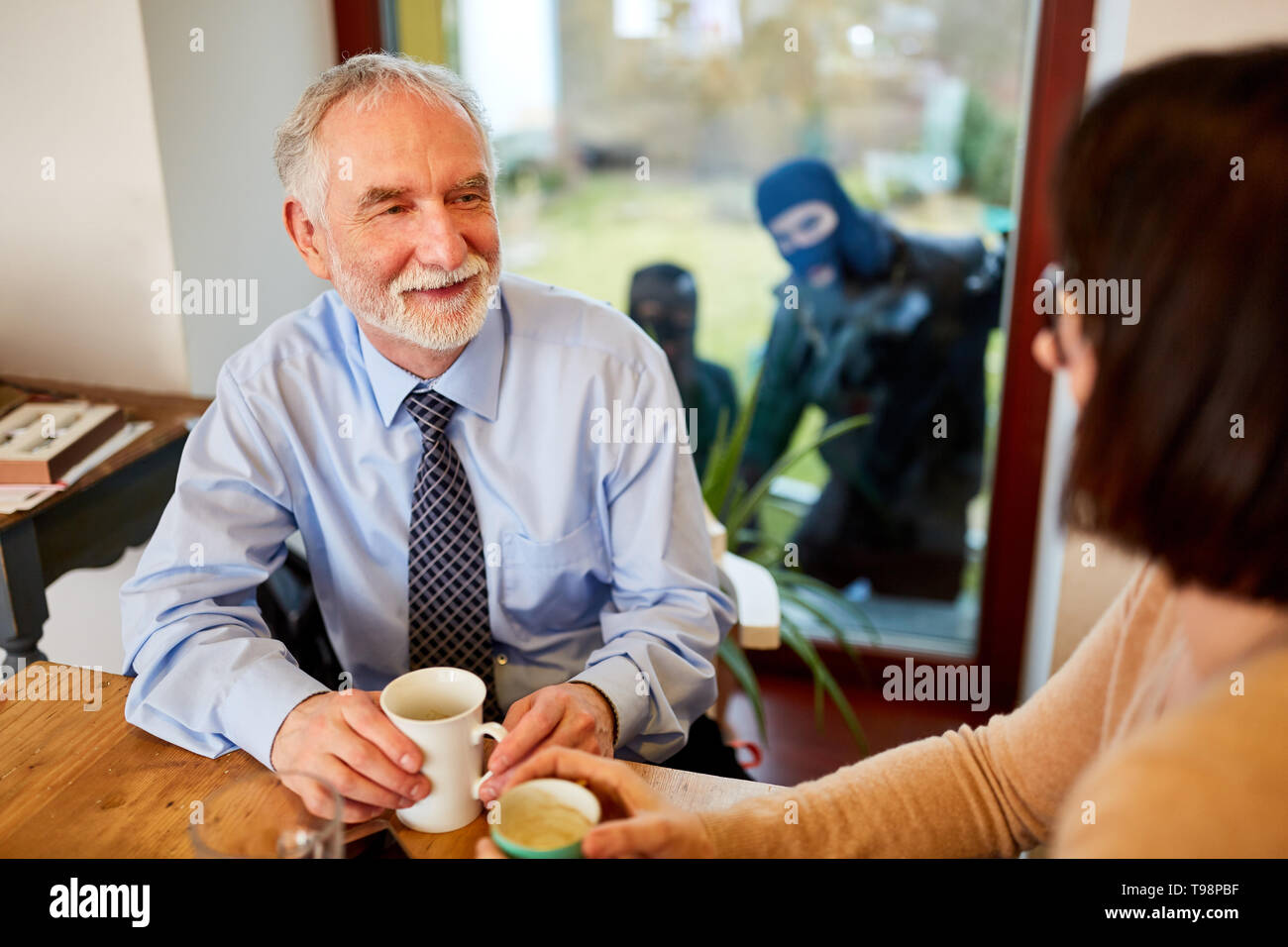 Two burglars watch a couple in the kitchen through a window Stock Photo