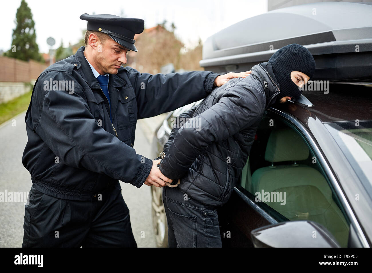 Police officer arrests car thief in the act and handcuffs him on arrest Stock Photo