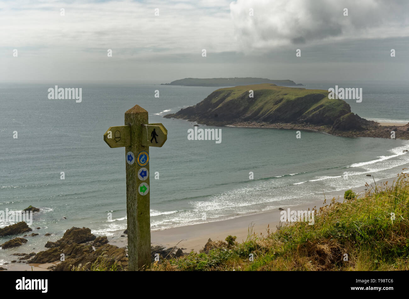 Looking past a Pembrokeshire Coast Path marker post to Gateholm Island and Skokholm, near Martin's Haven on the Marloes Peninsula in Wales Stock Photo