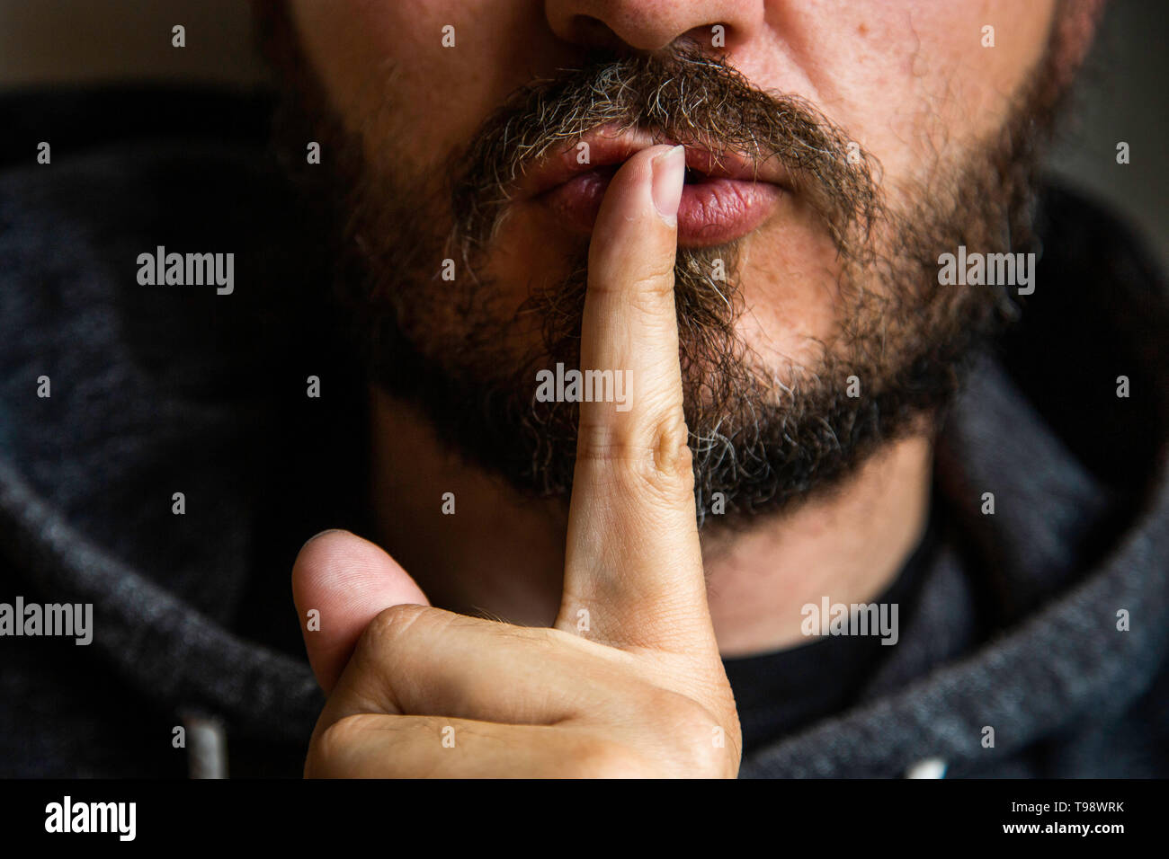 Don't speak, be quiet - close up portrait of bearded man on the door saying shhh. Finger on lips. Head and shoulders, no eyes. Danger. Stock Photo