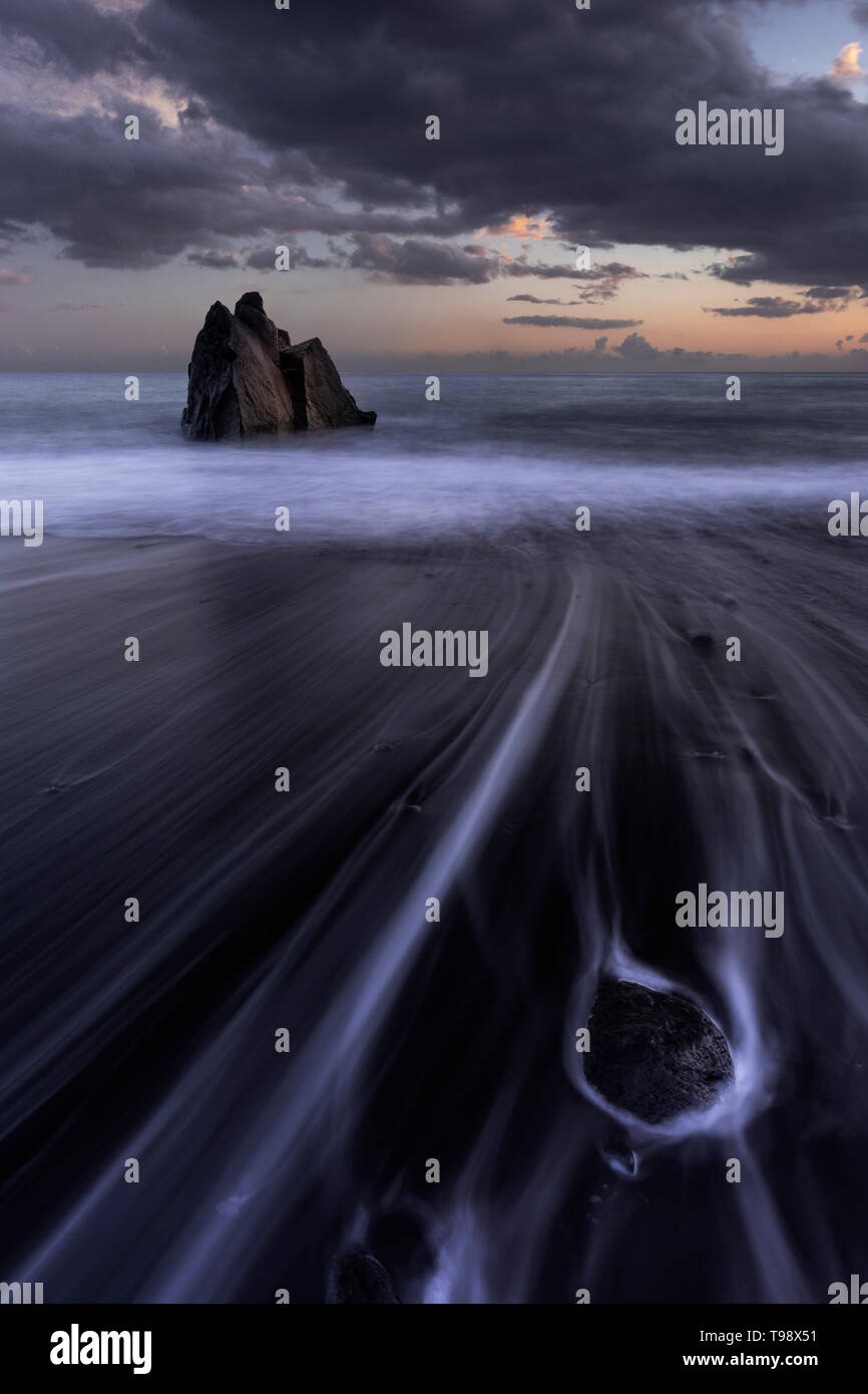 Praia Formosa at sunset, lava beach with a single rock on the left and rock formations on the right, Madeira, São Martinho, Portugal Stock Photo