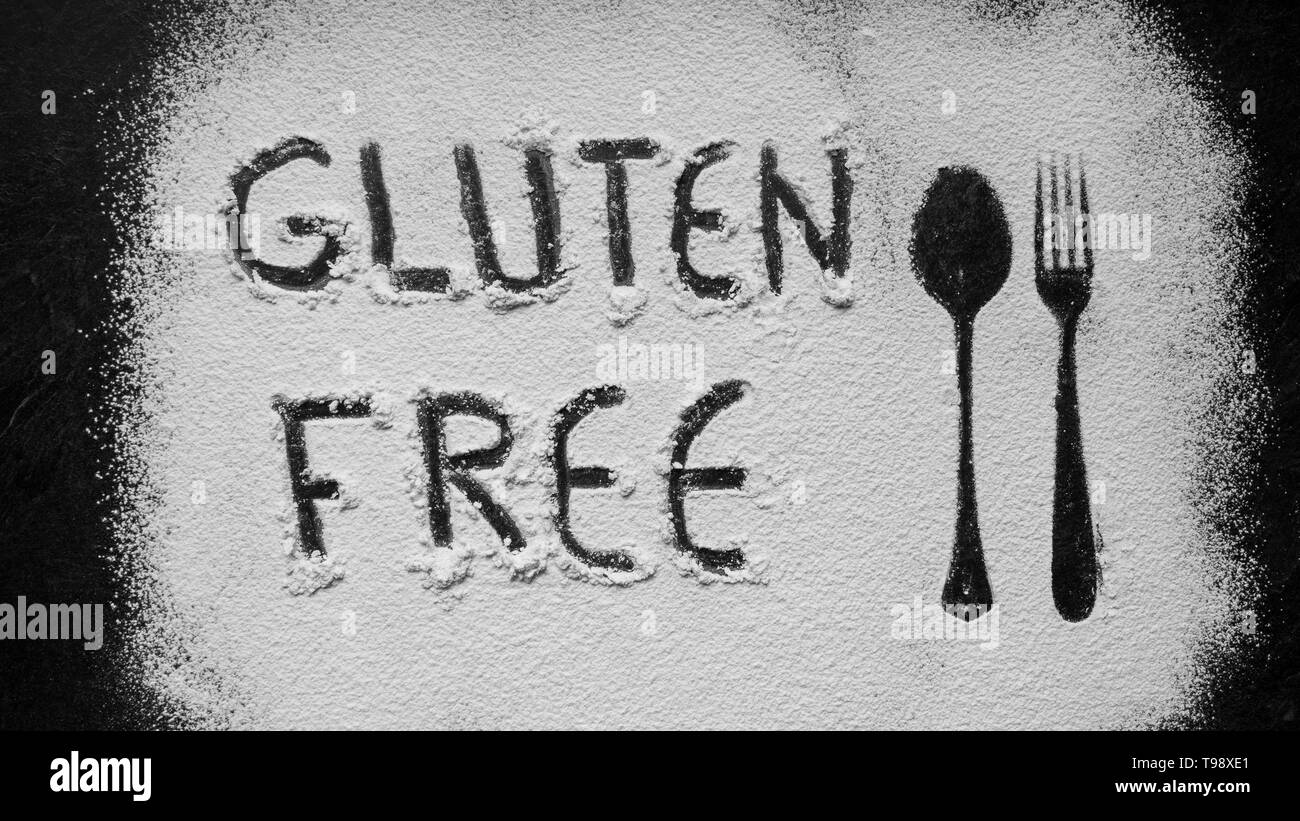 Gluten free flour with text gluten free in English language with spoon and fork silhouette made with flour on dark texture background,up horizontal vi Stock Photo