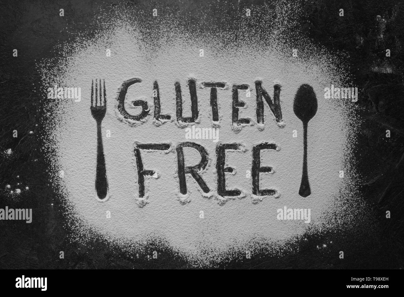 Gluten free flour with text gluten free in English language with spoon and fork silhouette made with flour on dark texture background,up horizontal vi Stock Photo
