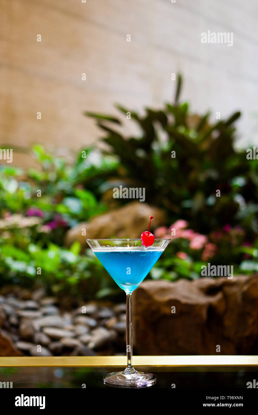 Blue cocktail decorated with red cherry in Martini glass garden background Stock Photo