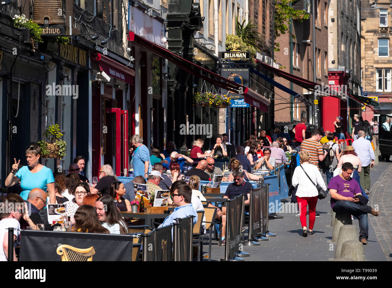 Many people drinking and eating outdoors in warm sunshine in bars and cafes on Grassmarket in Edinburgh Old town, Scotland, UK Stock Photo