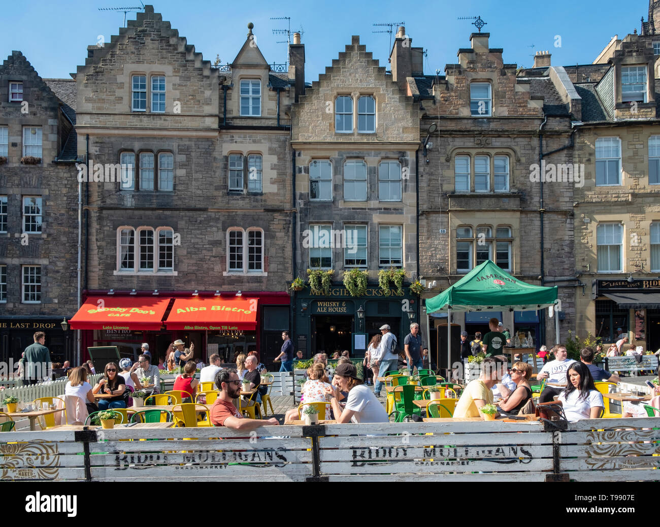 Many people drinking and eating outdoors in warm sunshine in bars and cafes on Grassmarket in Edinburgh Old town, Scotland, UK Stock Photo