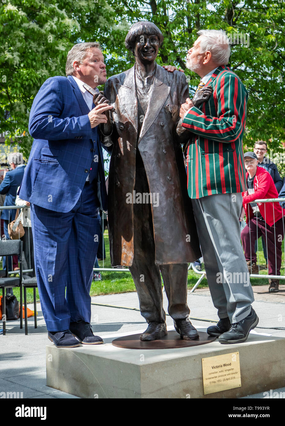 A life-size bronze statue of the late comedian, writer and actor, Victoria Wood is given a flying kiss during its unveiling in Bury town centre by comedian Ted Robbins (left) and her brother Chris Foote Wood. Stock Photo
