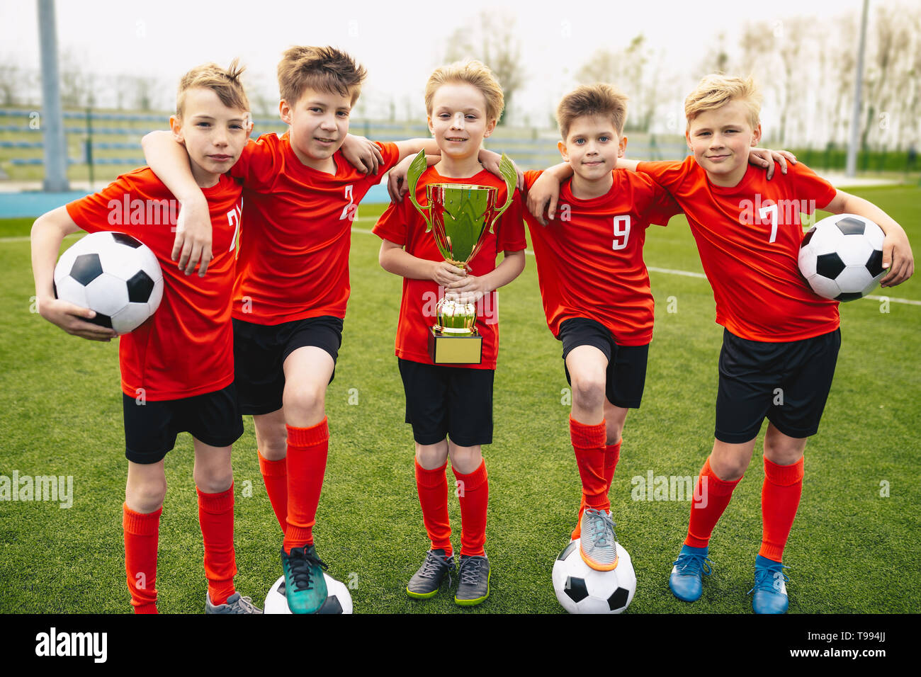 Happy Young Boys In Football Team. Kids in School Soccer Sports Team Holding Golden Trophy and Soccer Balls. Group Of Children In Soccer Team Having F Stock Photo
