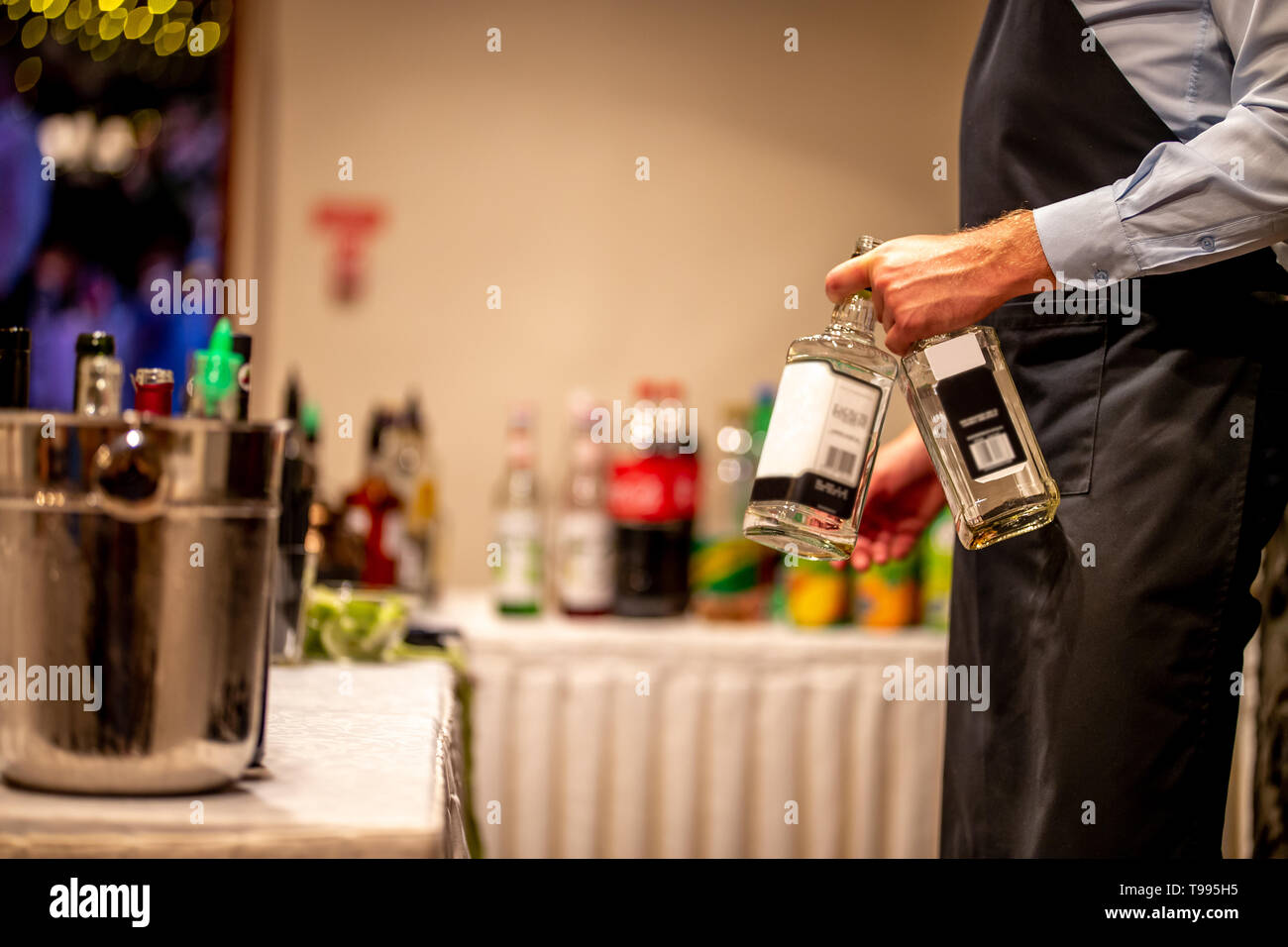 Waiter holds two whiskey bottles in hand. Waiter with two whiskey bottles in wedding party. Ice bucket with wine bottles. Stock Photo