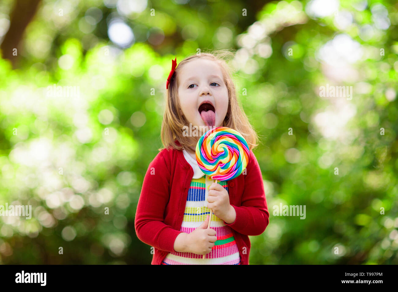 Cute little girl with big colorful lollipop. Child eating sweet candy