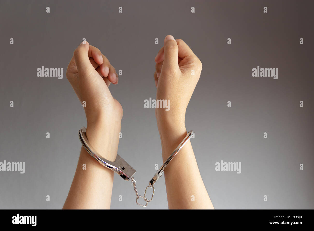 closeup of two hands of a man with handcuffs on a grey vignette background Stock Photo