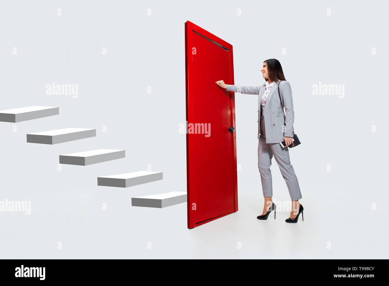 Knocking in emptiness. Young woman in grey suit trying to open the red door in career ladder, but it's closed. No way for motivation. Concept of office worker's troubles, business, problems, stress. Stock Photo