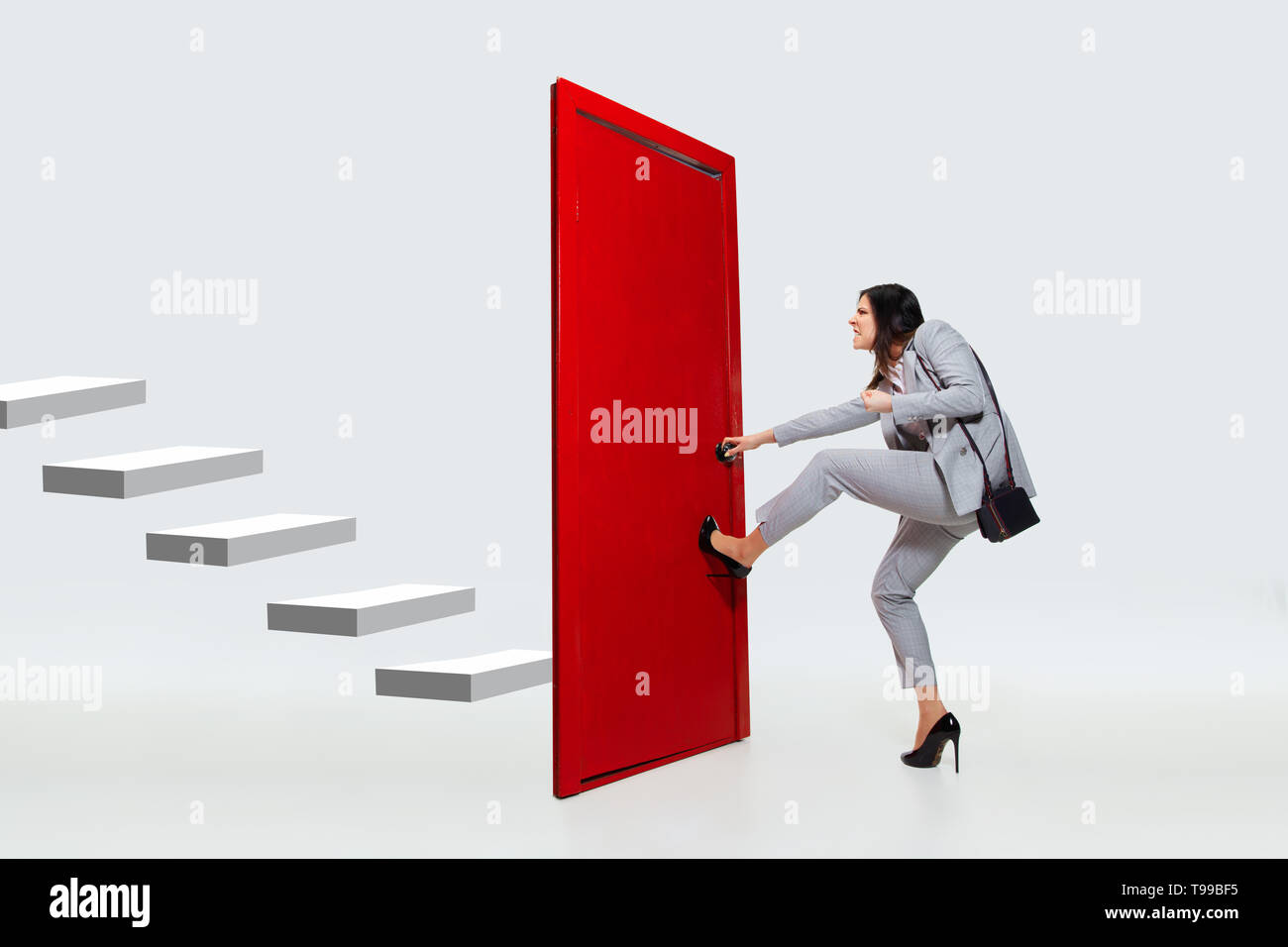 Knocking in emptiness. Young woman in grey suit trying to open the red door in career ladder, but it's closed. No way for motivation. Concept of office worker's troubles, business, problems, stress. Stock Photo