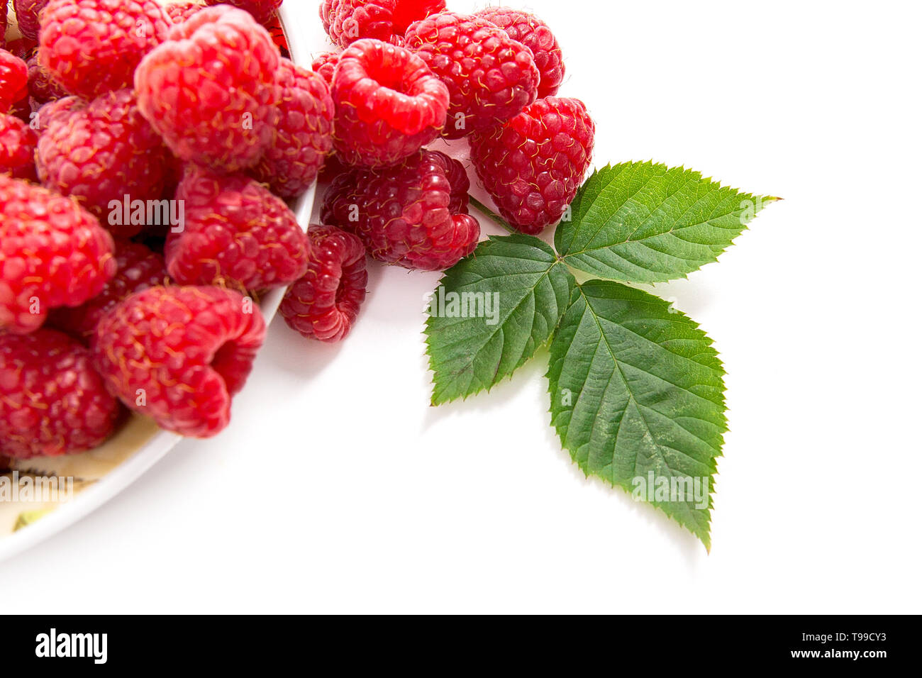 Close up view of plate with fresh raspberries fruits and big green leaf ...