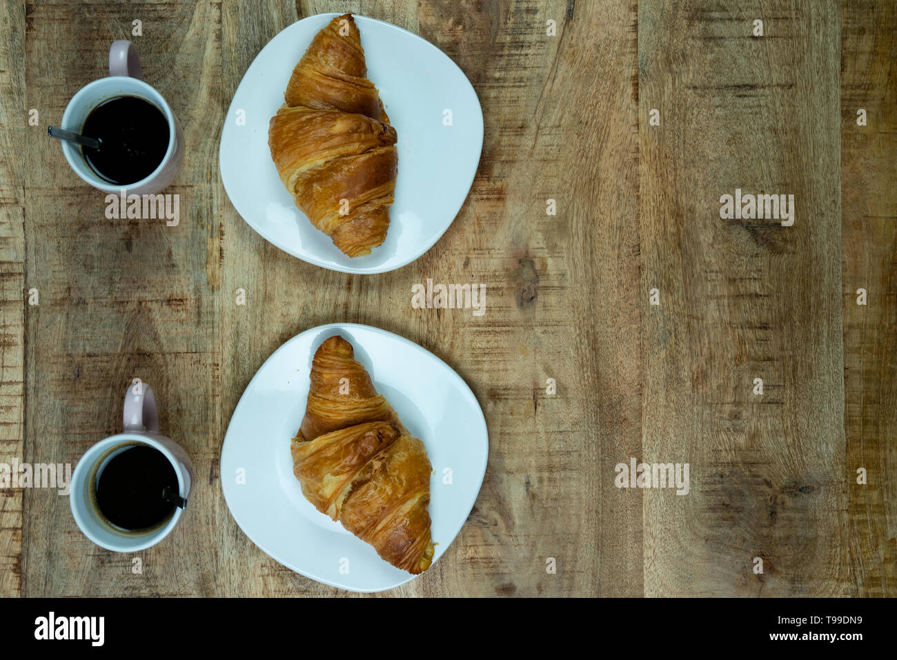 Breakfast or lunch for two. Freshly baked Croissants on a plate with coffee. On a wooden background, top view Stock Photo