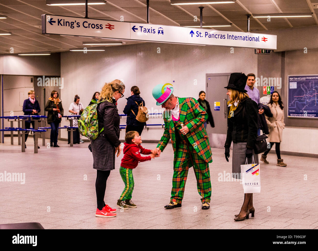Young child with mother, shaking hands with man dressed in clown suit, Kings Cross underground station, London, England, UK Stock Photo