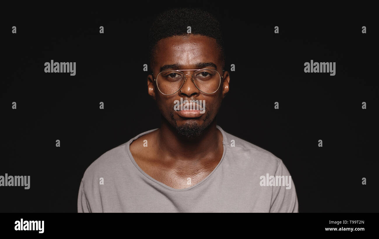 African male in eyeglasses and tshirt isolated on black background. Close up of african man looking at camera. Stock Photo