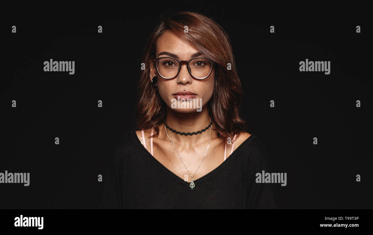 Woman in eyeglasses isolated on black background. Portrait of a fashionable woman with pierced lips looking at camera. Stock Photo