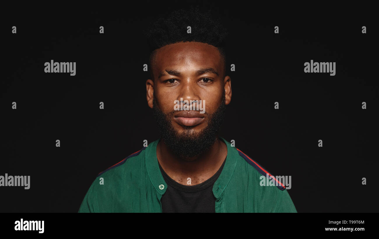 Portrait of african male looking at camera. African man with beard and spiky hair style isolated on black background. Stock Photo