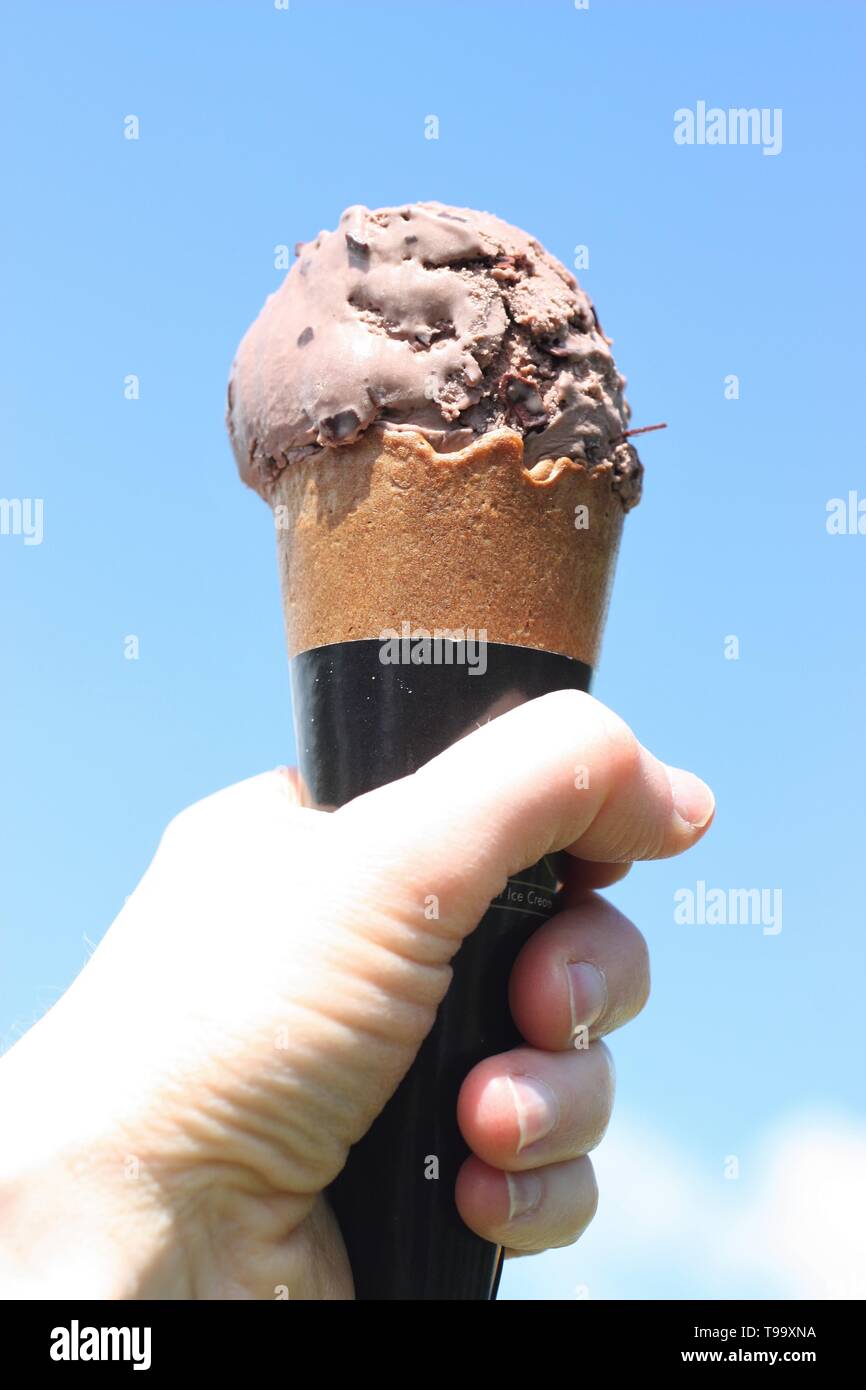 Hand holding a chocolate ice cream in a cone with blue sky behind Stock ...