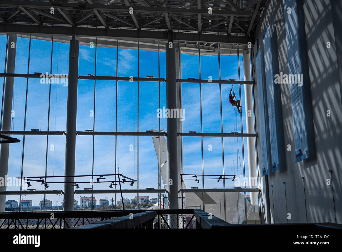 Industrial climber hangs from ropes inside shopping center or exhibition hall building against the blue sky, plenty of free space to sign Stock Photo