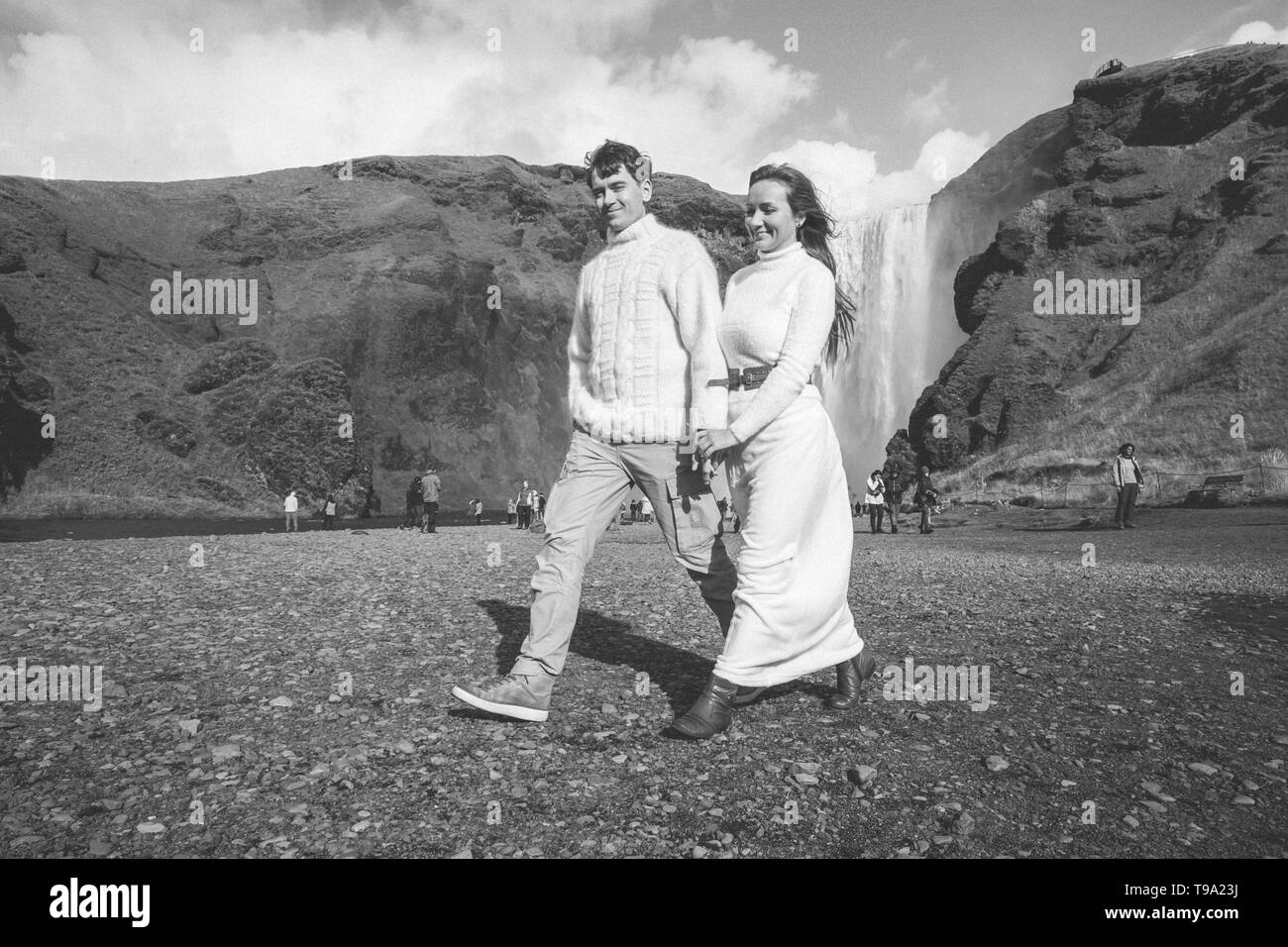 A young smiling couple in warm wedding outfit in front of a waterfall. Closeup  Stock Photo