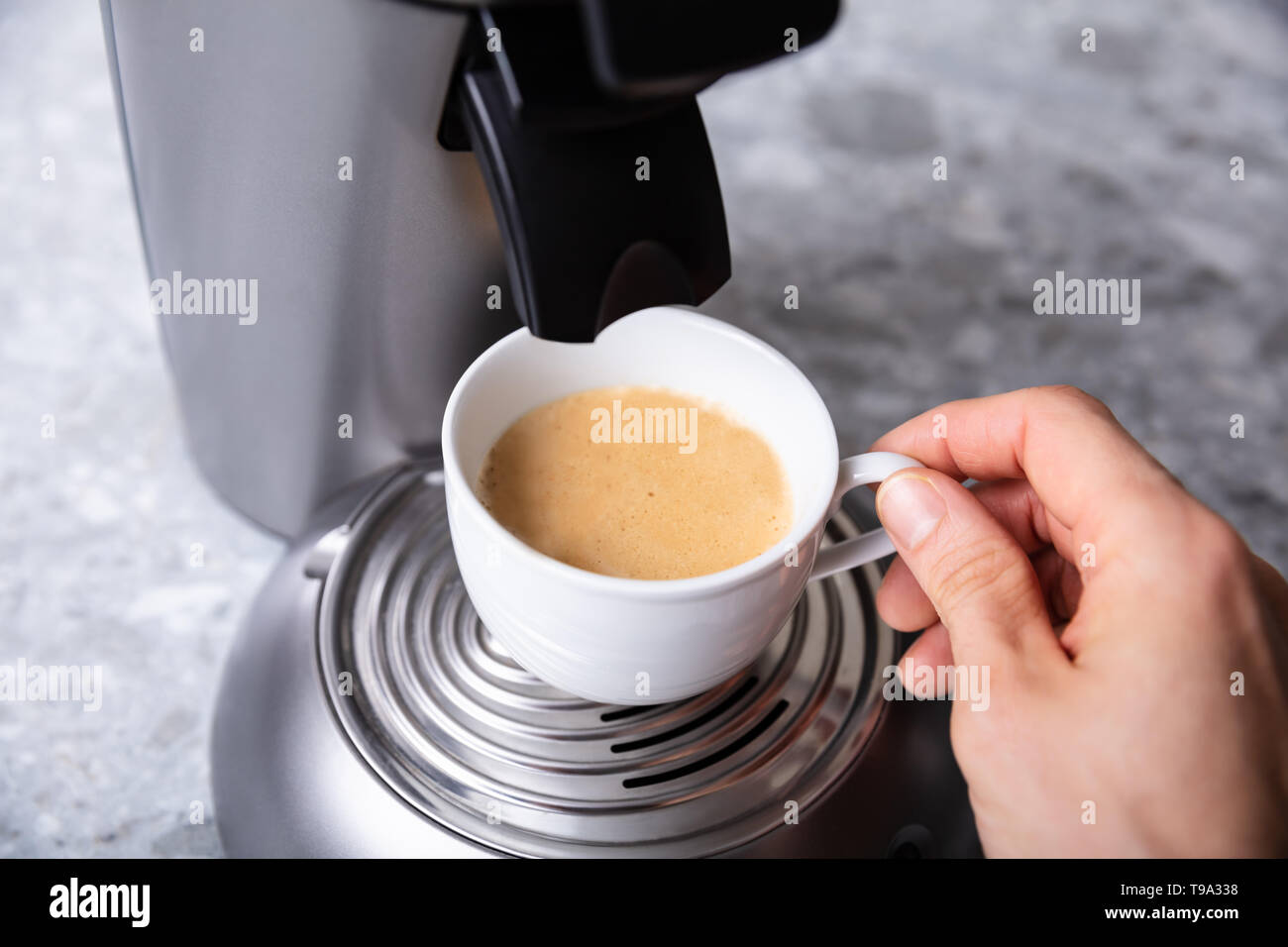 Closeup Of Person's Hand Holding Coffee Cup Under Coffee Maker Over