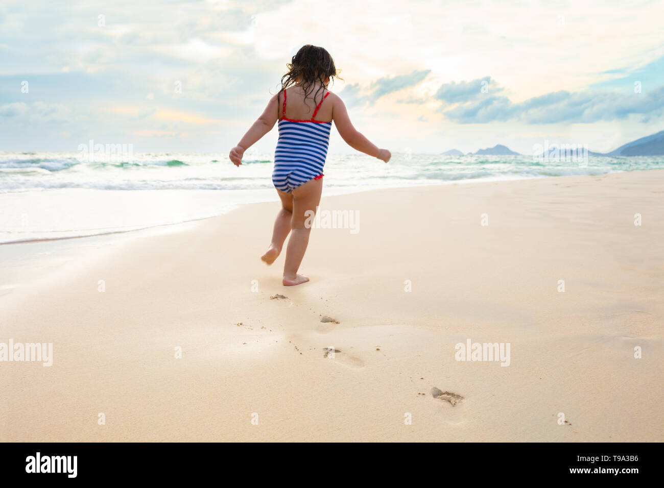 Little Girl In Bikini Running On The Idyllic Sandy Beach Near The