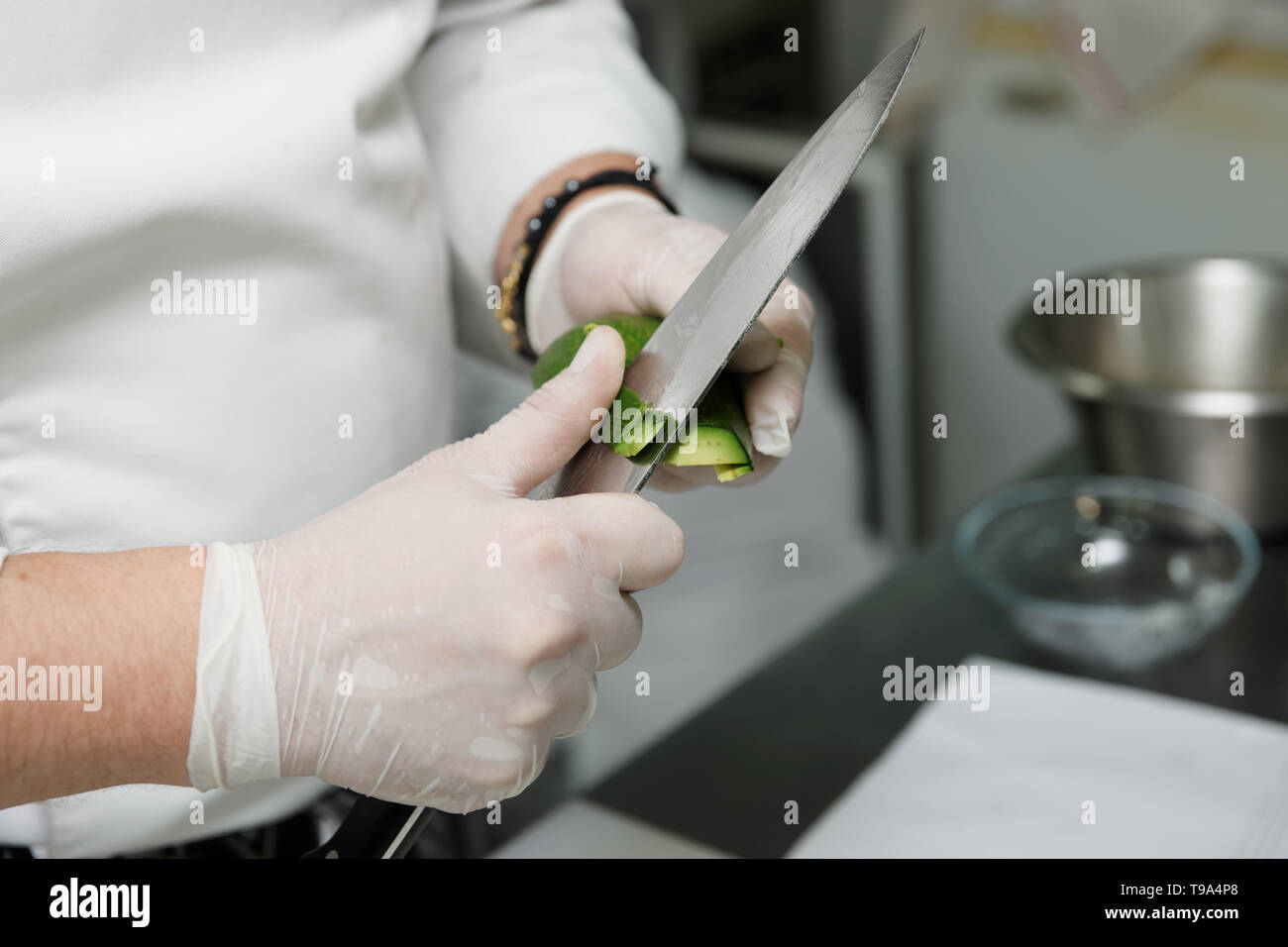 Chef is peeling avocado with knife in kommercial kitchen Stock Photo