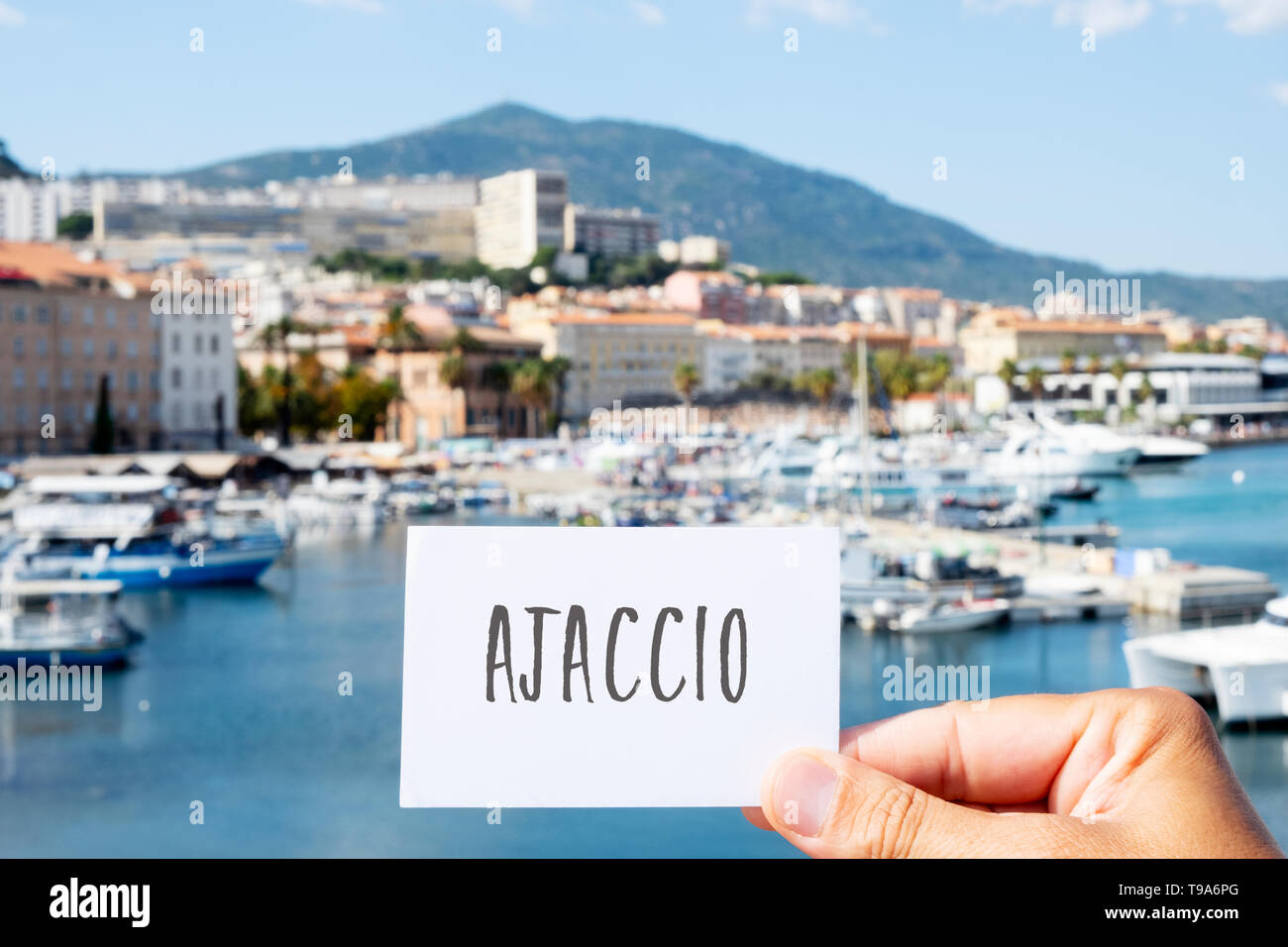 closeup of the hand of a young caucasian man holding a white signboard with the word Ajaccio written in it, at the Port of Ajaccio, in Corsica, France Stock Photo