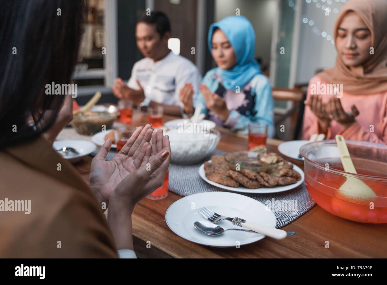Hijab women and a man pray together before meals, a fast breaking meal served on a table in backyard Stock Photo