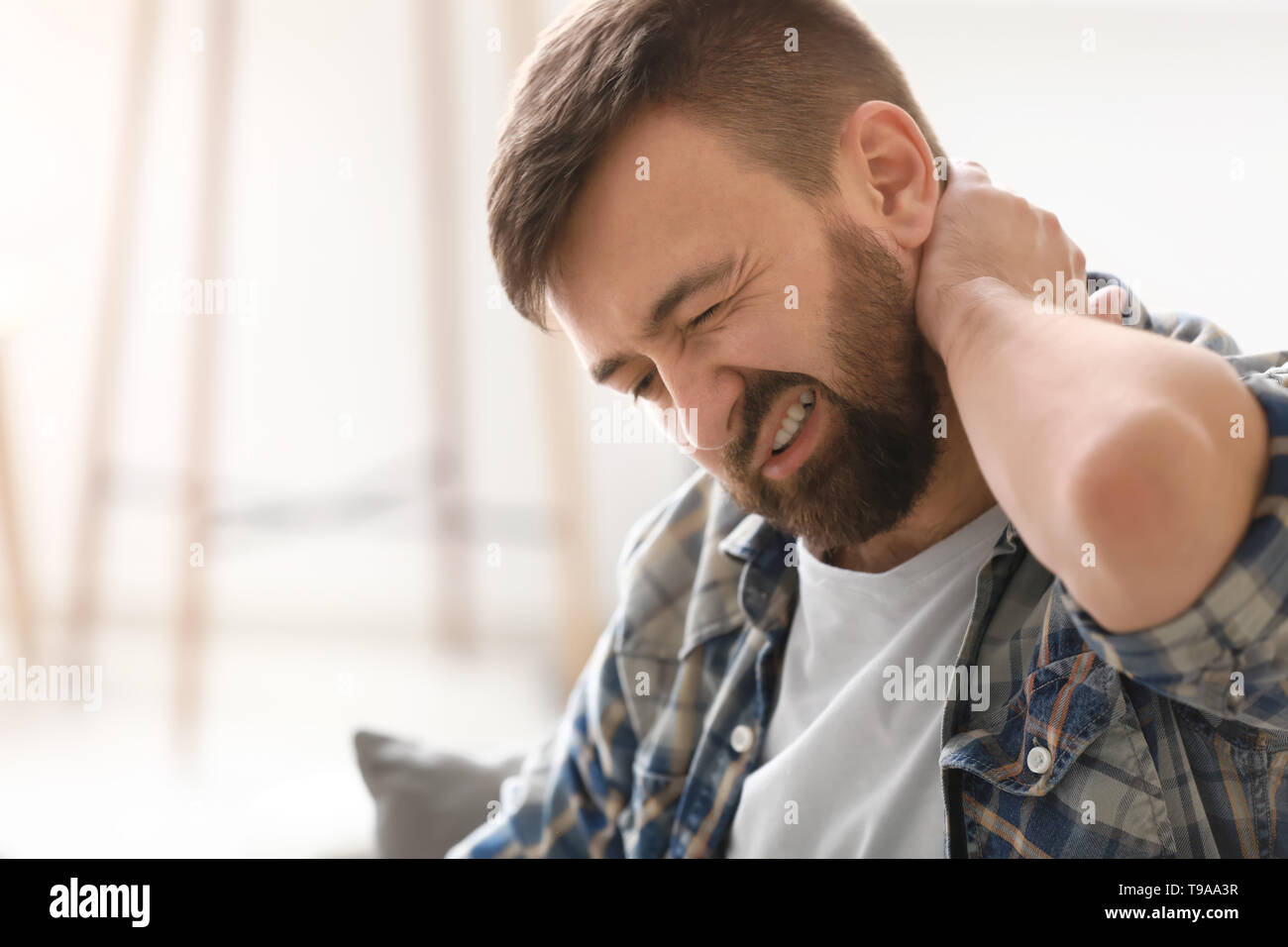 Man suffering from neck pain at home Stock Photo - Alamy