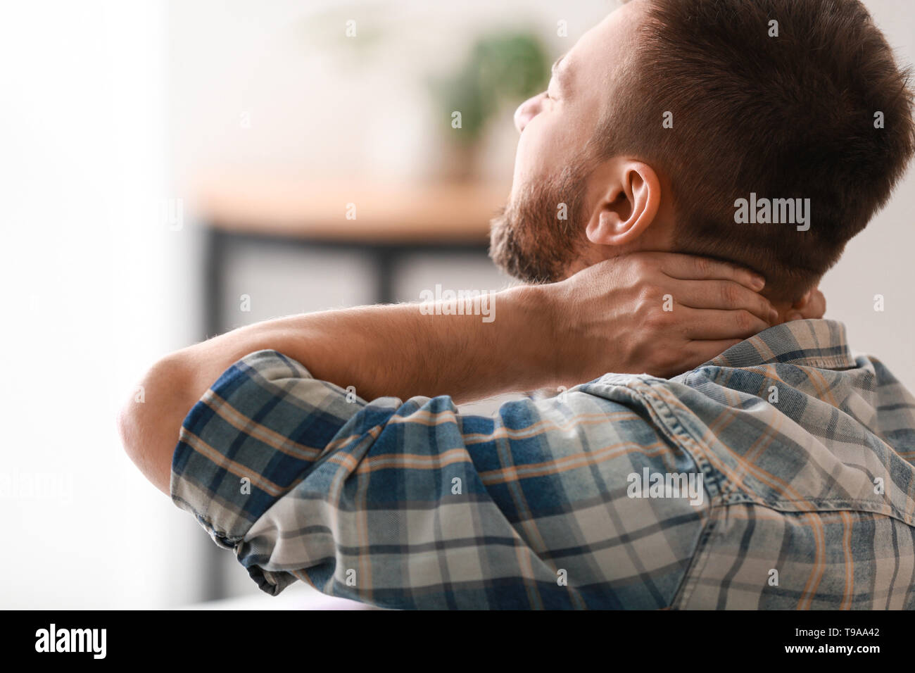 Man suffering from neck pain at home Stock Photo - Alamy