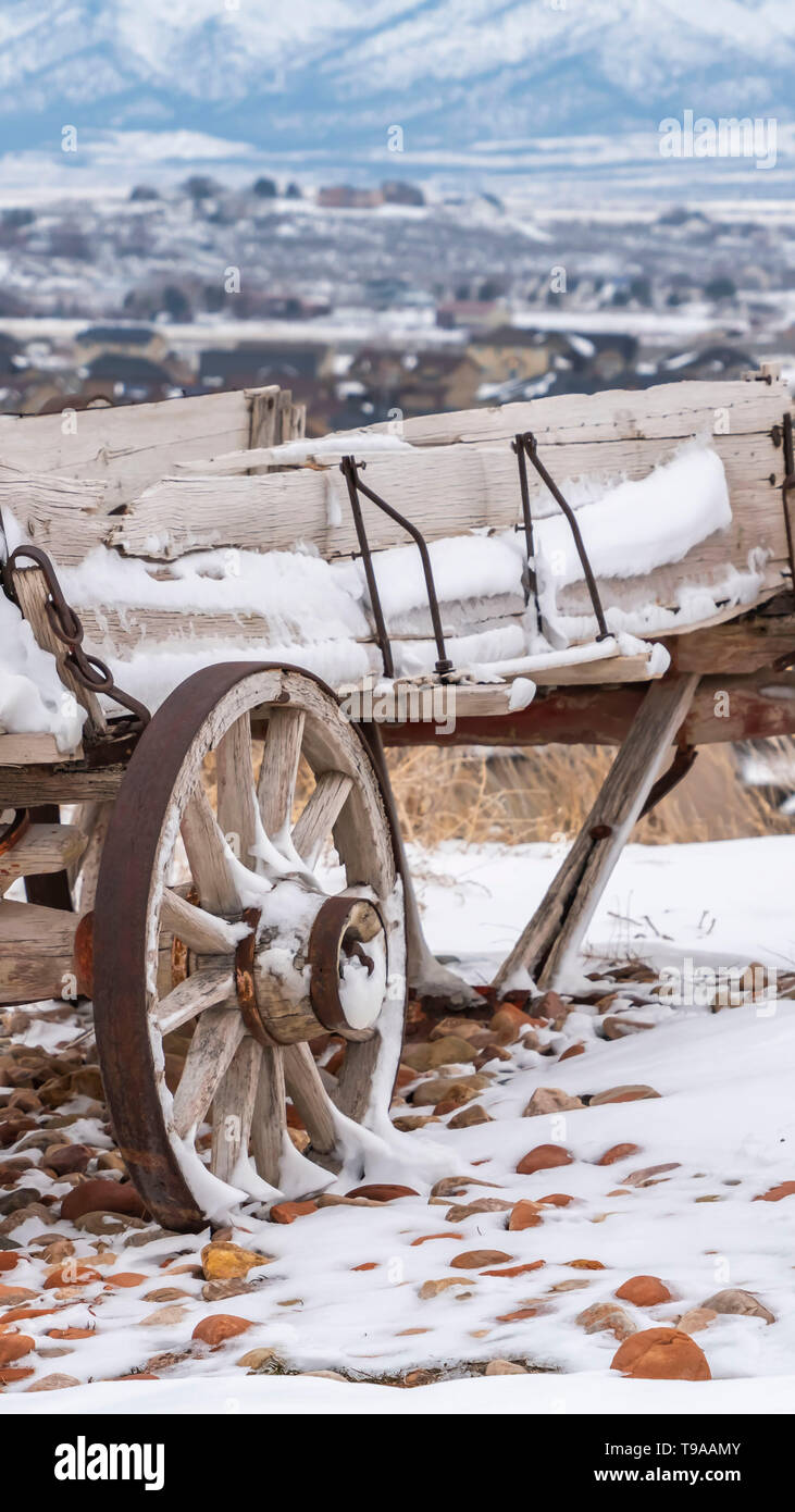 Vertical Old wooden wagon with chains and rusty wheels dusted with snow